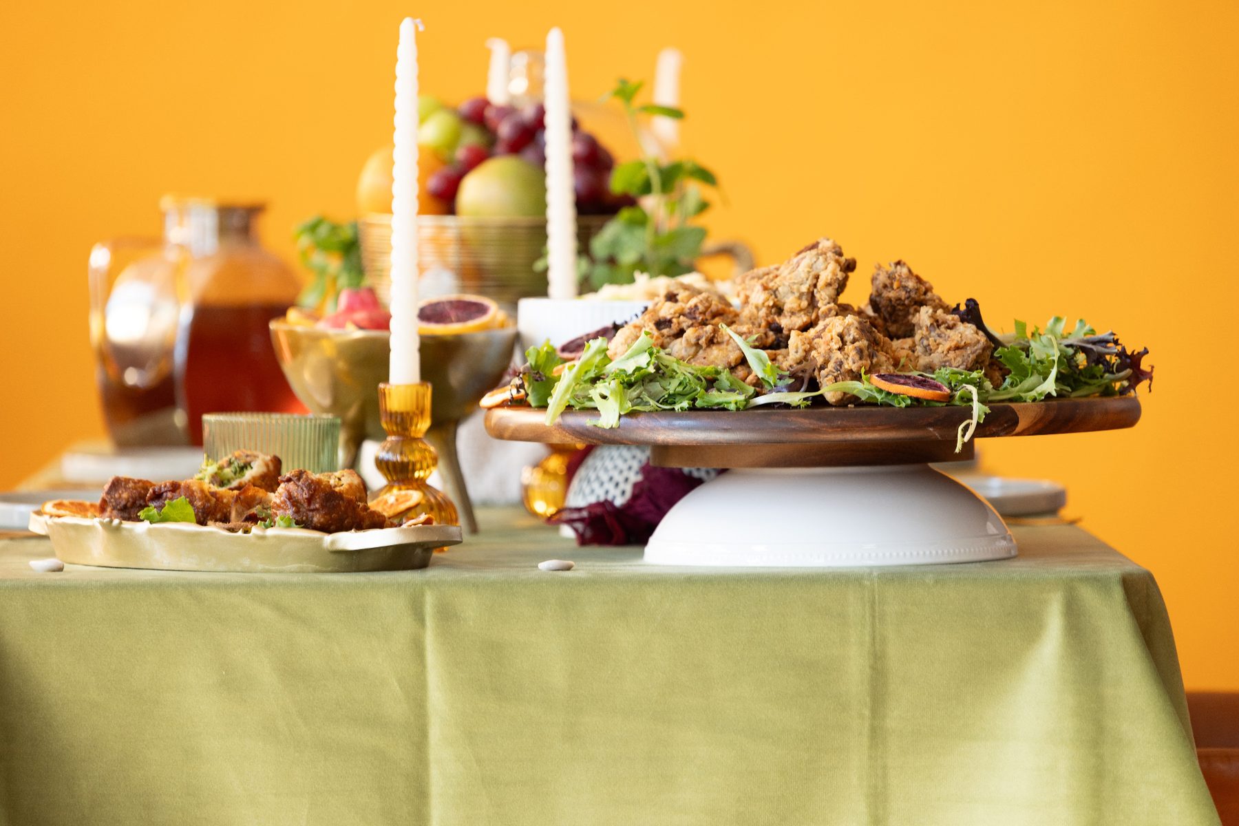 A banquet table set with lit candles, fruit and a raised platter
