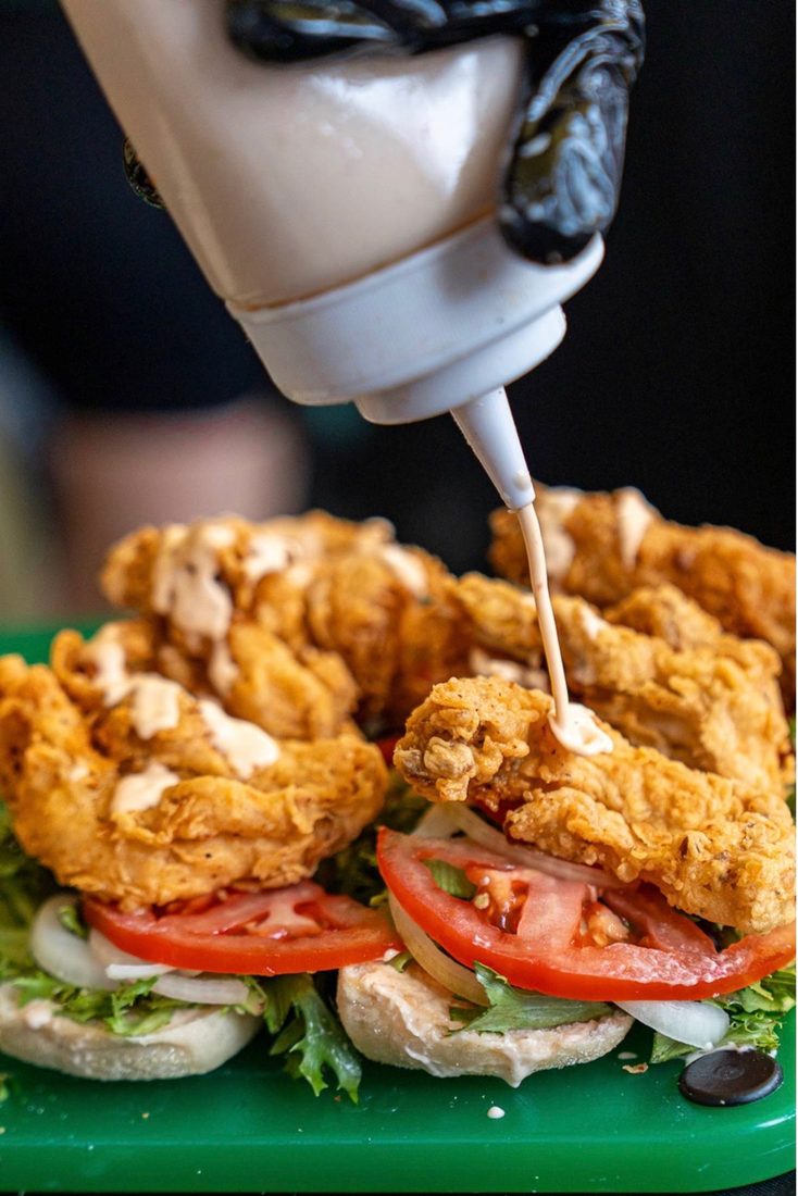 Sauce being squeezed over fried chicken in an open roll