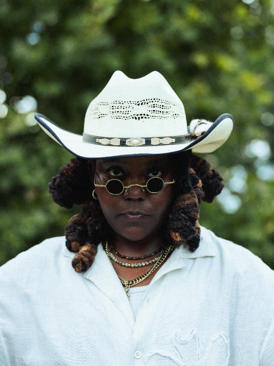 A STILL storyteller in a woven straw hat and round sunglasses, framed by soft green foliage